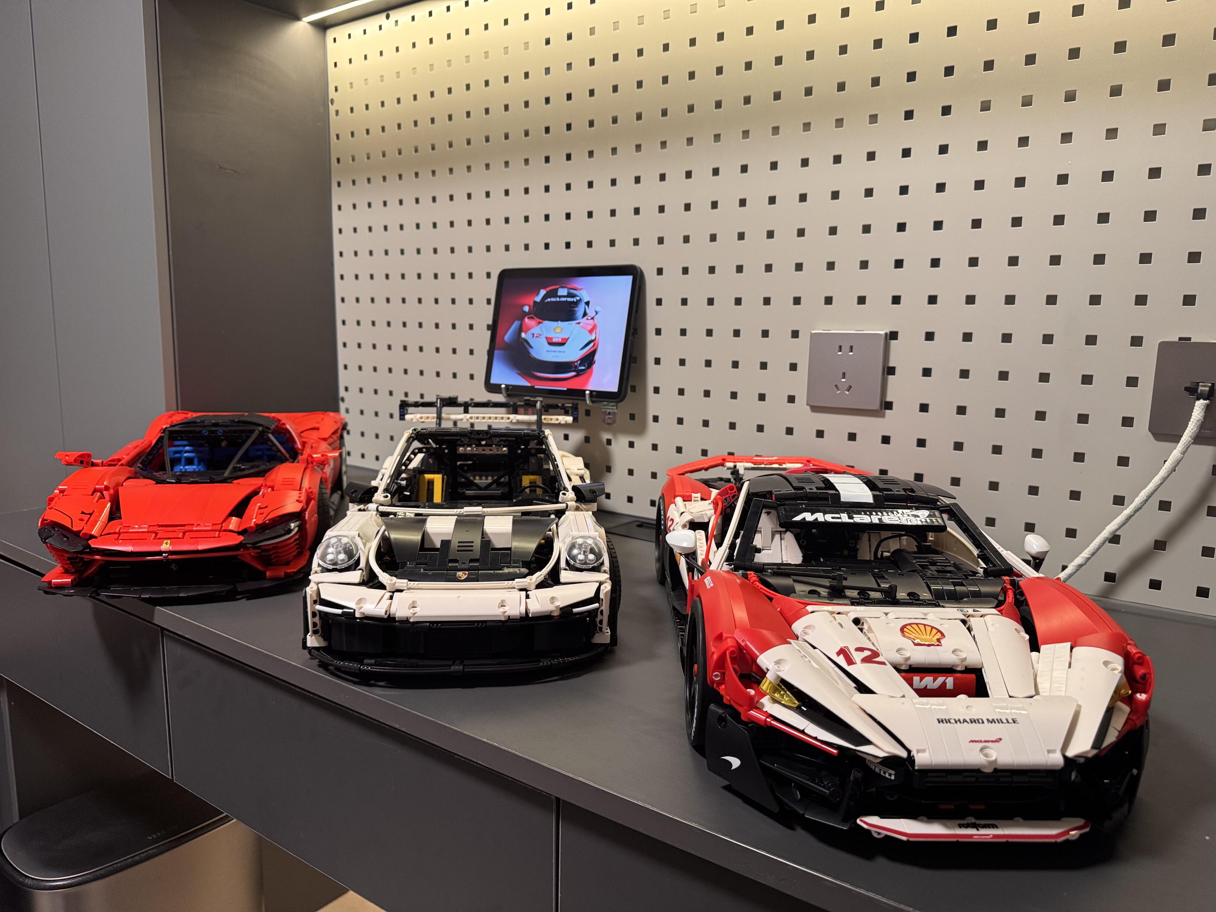 Three-car player collection — red Ferrari Daytona SP3, white Porsche 911 and red and white MOC 03 race livery on a display shelf